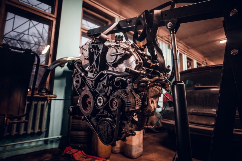 Female model with tattooed body wearing protective goggles next to a car engine